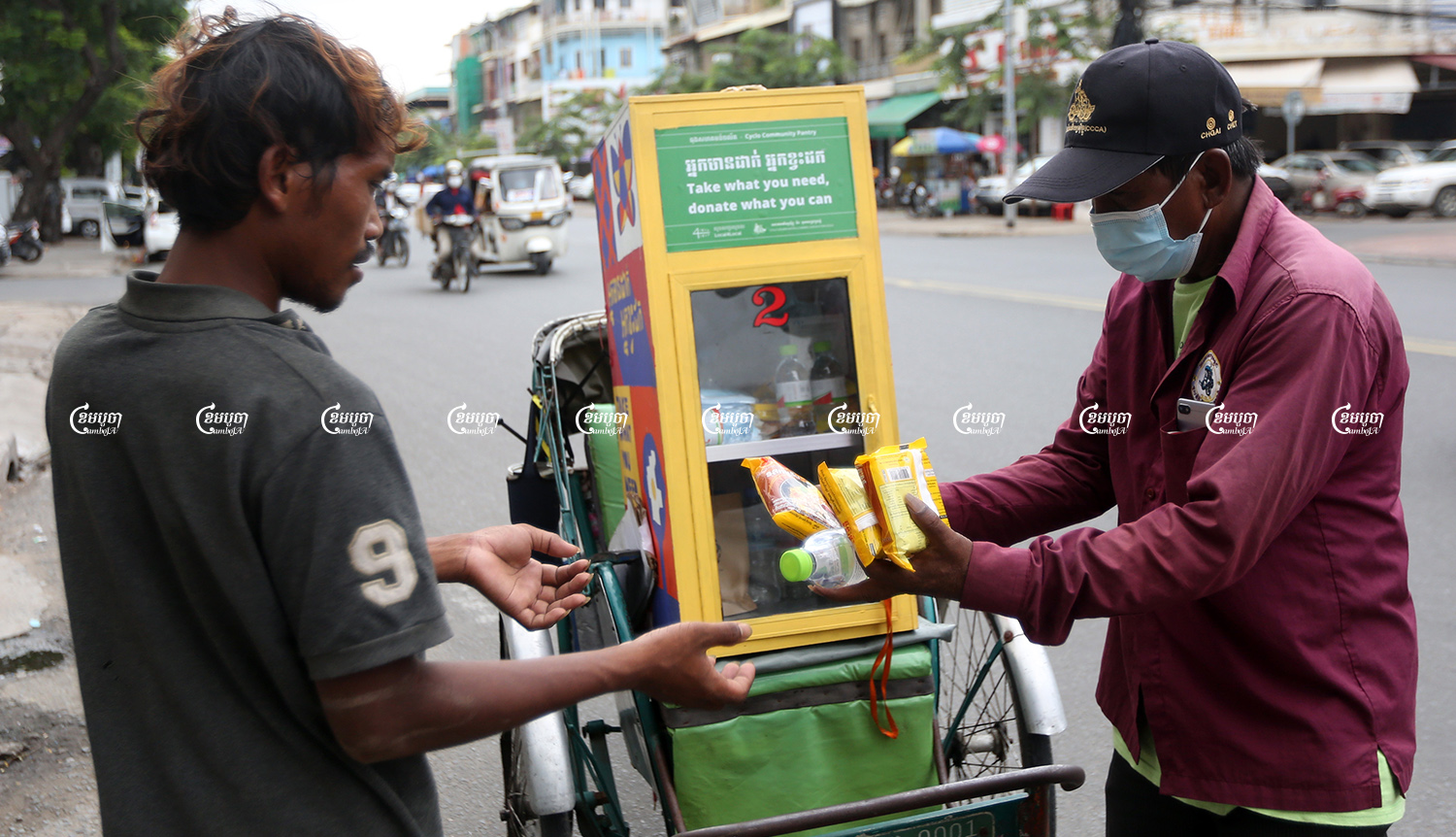 A cyclo driver offers food from his mobile pantry to a man in Phnom Penh, August 28, 2021. CamboJA/ Pring Samrang