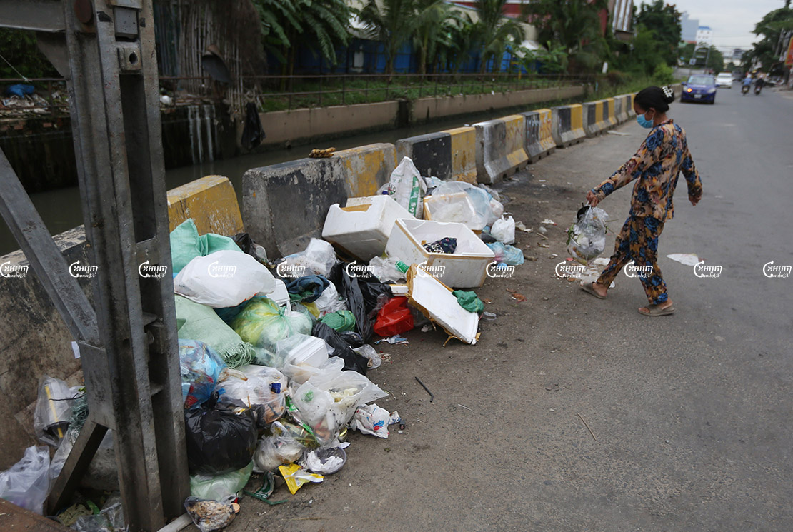 A woman drops garbage on a trash pile on a street in Phnom Penh, September 23, 2021. CamboJA/ Pring Samrang