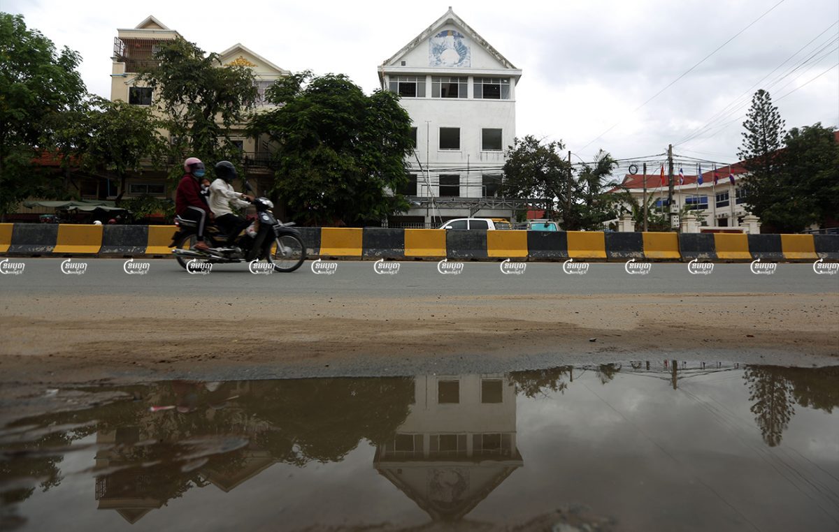 A man drives a motorcycle with a woman past the former Cambodia National Rescue Party headquarters in Phnom Penh. Picture taken May 24, 2021. CamboJA/ Pring Samrang