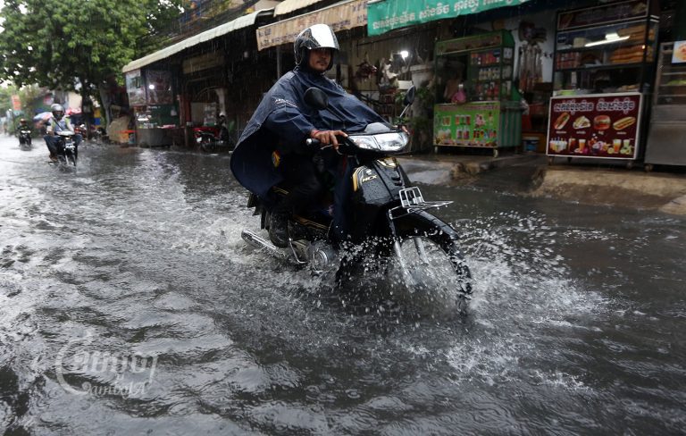 Residents drive motorcycles down a flooded road in Phnom Penh, Picture taken June 3, 2022. CamboJA/ Pring Samrang