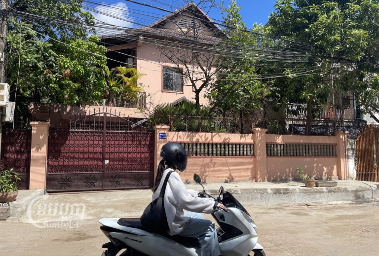A woman drives a motorcycle past the Phnom Penh home of opposition Candlelight Party vice president Son Chhay on November 28, 2022. The court has issued injunction to temporarily seize his properties. CamboJA/ Pring Samrang