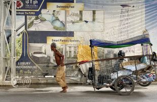 A man carries his scavenger cart past a condominium construction site in Phnom Penh on September 10, 2022. (CamboJA/Pring Samrang)