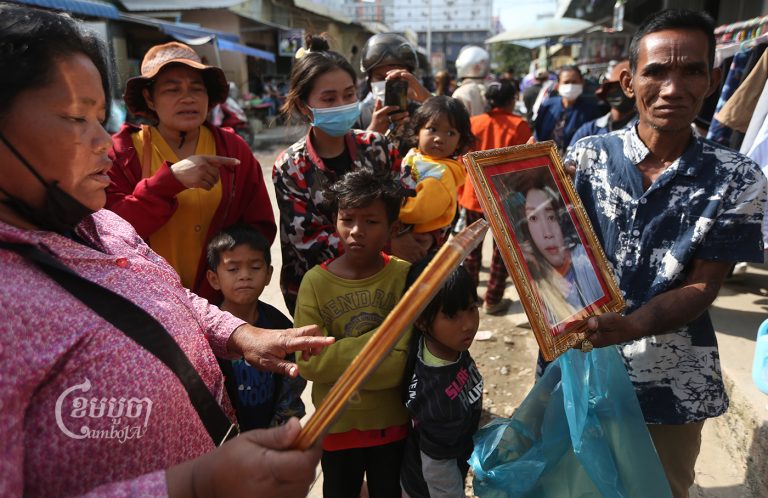 Waiting for information outside Trach pagoda near the site of the fire, Ban Doch (right) holds a portrait of his niece, a worker inside Grand Diamond City casino and hotel who was missing as of early afternoon on December 30, 2022. (CamboJA / Pring Samrang)