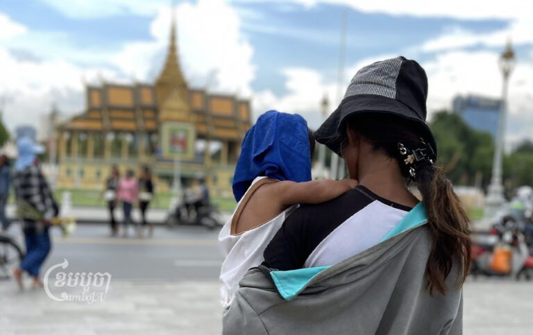 A woman carries a child in front of the Royal Palace in Phnom Penh on June 28, 2023. CamboJA/ Pring Samrang