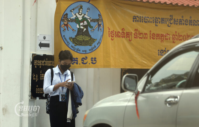 A student looks at her smartphone in front of the Boeng Keng Kang high school entrance in Phnom Penh on July 7, 2023. (CamboJA / Pring Samrang)