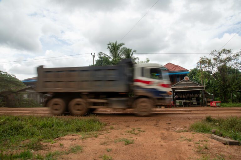 A Global Green truck loaded with iron ore passes through Rik Reay commune, kicking up dust, September 17, 2023. (CamboJA/Andrew Califf)
