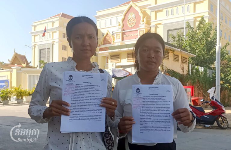 Boeng Tamok villagers Soeun Sreysoth and Sea Davy hold up their court warrants before entering Phnom Penh Municipal Court for questioning on December 14, 2023. (CamboJA/Phon Sothyroth)
