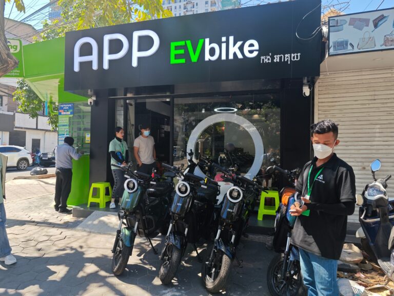 A storefront of an App EV Bike location, with electric bikes and people standing in front.
