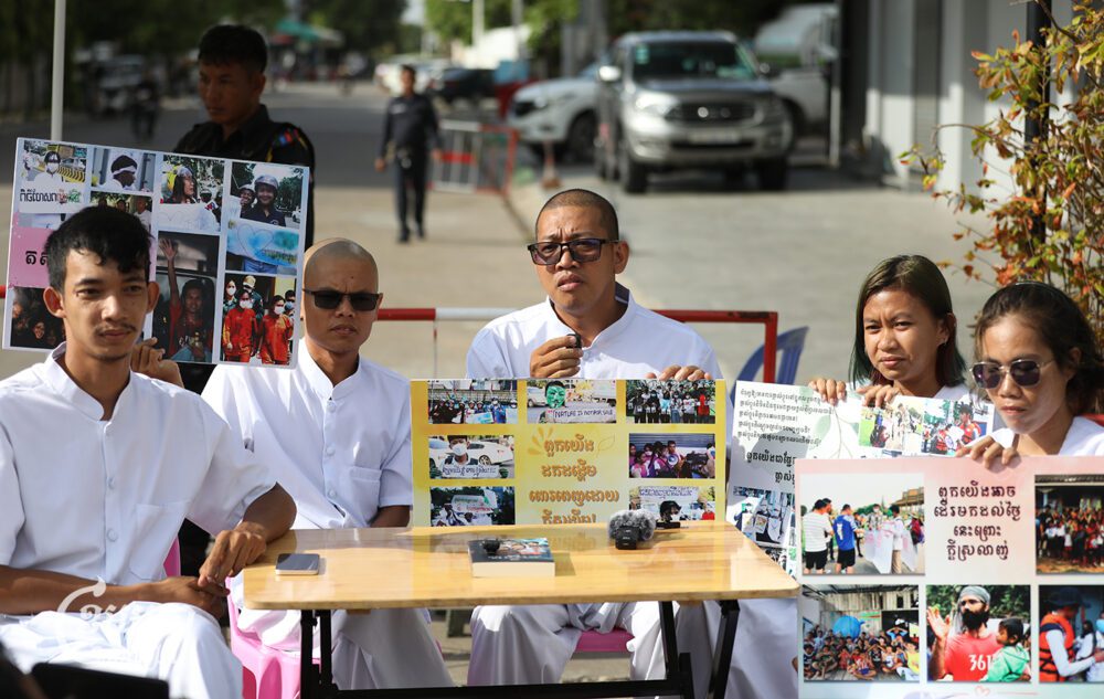 Five environmental activists produce a live podcast outside the barricade set up by the authorities to block supporters from entering the Phnom Penh Municipal Court before their hearing on June 11, 2024. (CamboJA/Pring Samrang)
