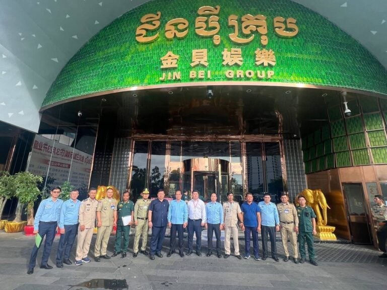 Authorities pose in front of a building with a Khmer and Chinese signboard bearing Jin Bei Group’s name on November 2, 2025. (CGMC Facebook page)